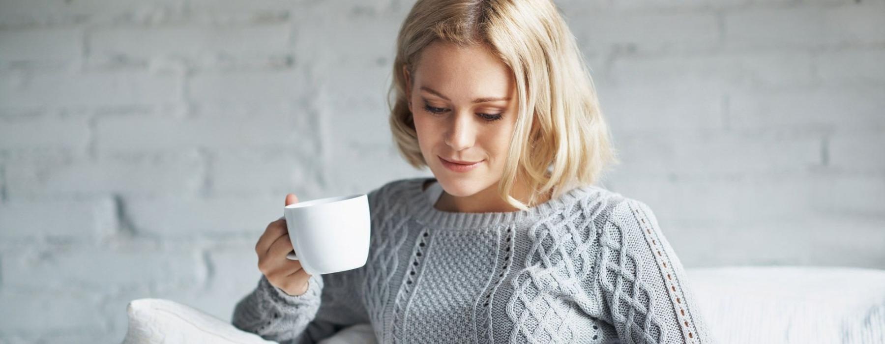 a woman sits on a couch with a cup of coffee and looks at her tablet