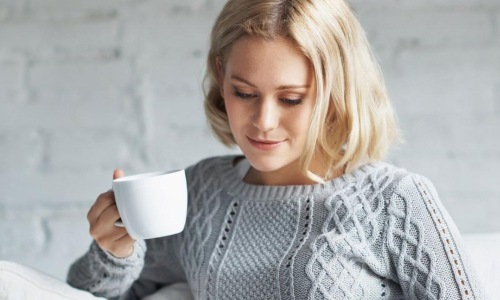 a woman sits on a couch with a cup of coffee and looks at her tablet